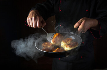 The chef is preparing oladki in a frying pan. The concept of preparing Ukrainian national dish or bliny in the kitchen. Black space for recipe or menu