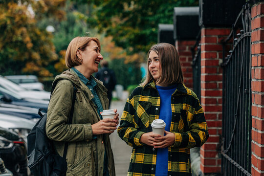 Smiling mother talking to daughter and holding coffee cup at sidewalk