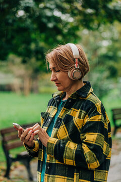 Woman wearing wireless headphones and using smart phone in park