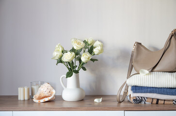 knitted clothing and white roses in jug on modern dresser