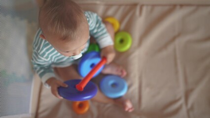 Fototapeta na wymiar baby toddler plays with a toy pyramid sits in a crib arena. happy family kid lifestyle dream concept. baby toddler development of fine motor skills plays with pyramid rings in kindergarten