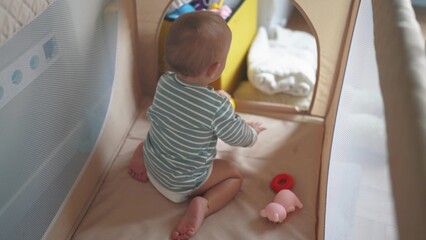 baby crawling first steps. baby toddler gets out of the playpen crib learns to crawl plays. happy family kid dream concept. baby toddler play in crib playpen lifestyle indoors in kindergarten - obrazy, fototapety, plakaty