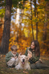 Smiling beautiful family of four walking in the park with a happy golden retriever and enjoying the beautiful autumn nature. 