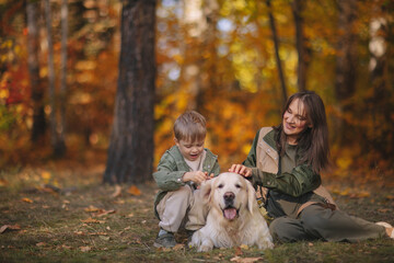 Smiling beautiful family of four walking in the park with a happy golden retriever and enjoying the beautiful autumn nature. 