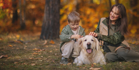 Smiling beautiful family of four walking in the park with a happy golden retriever and enjoying the beautiful autumn nature.