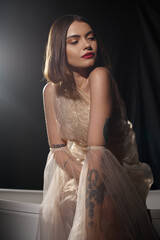 brunette young woman posing in romantic transparent dress near bathtub with black backdrop