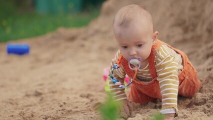 baby baby close-up in colorful sandbox. happy family kid dream concept. boy is playing on the playground. kid is sitting in sand playing with his toys. small child climbs on the yellow sand lifestyle