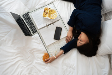 Busy and tired businesswoman eating bread for breakfast in bed at home and working to deliver...