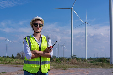 engineer with turbine in background. Service engineers checking wind turbine on tablet on  wind turbine farm Power Generator  on background Station on mountain, Thailand people
