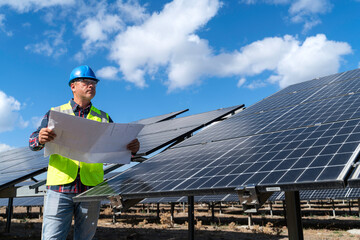 Portrait of male manager engineer in safety helmet checking with blueprint an operation of solar...