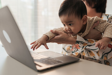 A little boy Asian baby is disturbing his mother while she is working at home. Asian mother...