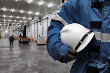 Officer holding hardhat for dangerous accident protection in warehouse during work. Cold room storage and freezing warehouse. Cold Storage Room Service, Inventory Management Concept.