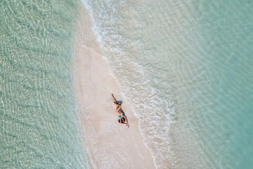 young woman tanning sunbathing woman wearing bikini at the beach on a white sand from above view from drone