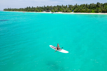 Aerial view of a woman on a white supboard in the turquoise waters of the Maldives