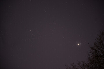 The planet Venus in the starry night sky in conjunction with the Pleiades Constellation. The group of stars The seven sisters observed from a dark place