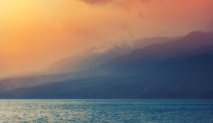 Fototapeta premium sea or lake in foggy haze at the foot of beautiful mountains at sunset