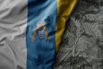 waving flag of canary islands on the old khaki texture background. military concept.