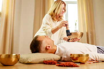 Woman playing on a tibetian singing bowl maling massage meditation for a man