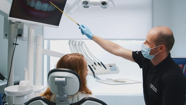 Middle aged dentist demonstrating x-ray image to female patient explaining dental treatment measures in stomatology clinic. Modern dental office. Hygiene. Medicine.