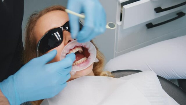 Hands of tooth doctor inserting dental retractor in young woman's mouth preparing medication treatment in the office. Stomatology clinic. Oral hygiene. Healthcare.