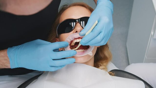 Professional caucasian dentist examines teeth of young female patient. Orthodontist installing dental retractor in mouth for teeth whitening. Treatment. Medicine.