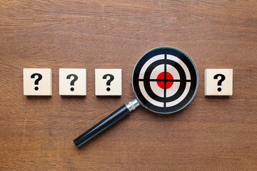 Many question mark icons on wooden blocks with magnifying glass with target inside, what's your target, find the audience