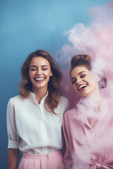 Portrait of two happy women on a blue background filled with light pink smoke.Pastel colors,minimal concept.