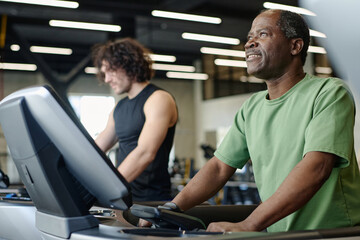 Fototapeta na wymiar African american man walking on treadmill at gym with caucasian sportsman training on background