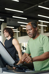 Fototapeta na wymiar Black man about to press key on treadmill at gym with caucasian man training on background