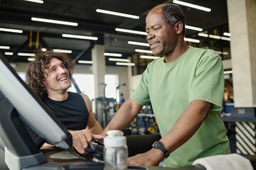 Elderly black man walking on treadmill at gym with young caucasian athlete standing next to him