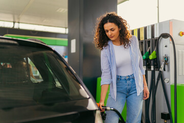 Young woman with curly hair refueling car at a self service gas station