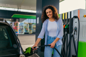 A beautiful woman with curly hair is filling her car tank while taking a break on her road trip