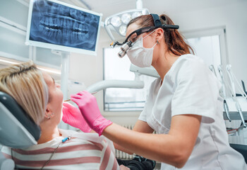 Dentist female doctor dressed uniform in magnifying glasses performing preventive dental care....