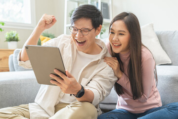 Happy excited, smiling asian young couple love using tablet pc, great deal or business success, received or getting cash back, tax refund, good news by mail while sitting on floor at home. - obrazy, fototapety, plakaty