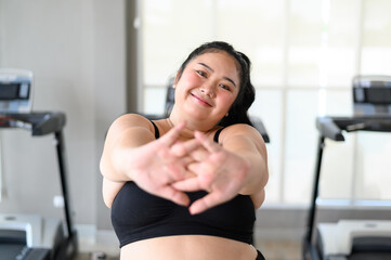 Happy Overweight Asian woman stretching before some main exercises in gym. Weight loss workout, healthy lifestyle concept.