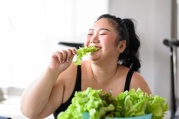 Overweight Asian female happy to eat organic green vegetable salad for healthy in gym. Weight loss workout, healthy lifestyle concept.