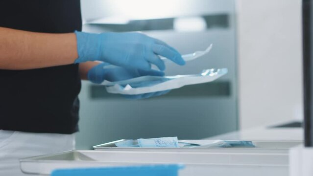 The doctor will put dental instruments for sterilization in a steam autoclave. Close-up of female assistant in laboratory sorting medical instruments. Dental clinic concept.
