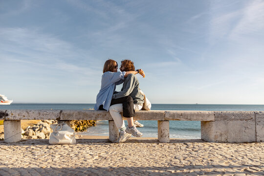Couple in love is hugging while sitting bench on beach near ocean. High quality photo