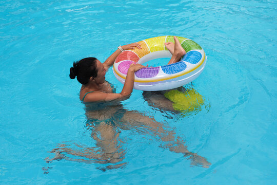 A boy grips a colorful float as his mother smiles; a sunny pool scene. This image ties to the joy of active parenting.