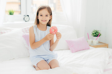 Obraz na płótnie Canvas Happy young girl holding a donut in a bright and cozy bedroom