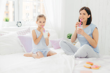 Obraz na płótnie Canvas Mother and daughter enjoying milkshakes in a bright bedroom setting