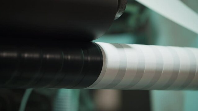 Industrial equipment covering up the steel tube with protective white tape. Industrial machine putting the corrosion-preventing tape on a tube. Industrial tape wrapped around the tube.