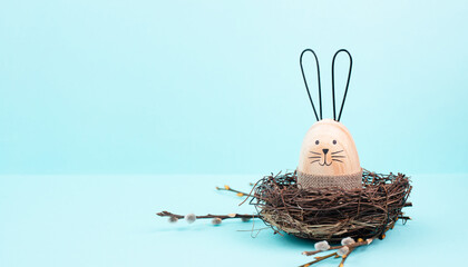 Easter bunny or rabbit sitting in a bird nest, willow branches, wooden egg, spring holiday, brown...