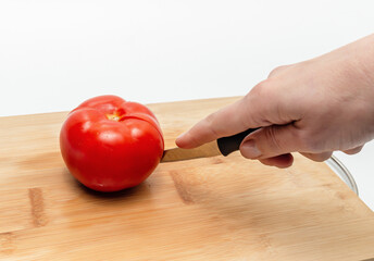 Cutting red tomato with knife into two halves on wooden kitchen board. Woman's hand cuts a tomato.