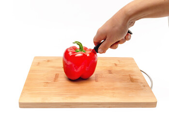 Cutting bell pepper with knife into two halves on a wooden kitchen board. Female hands. Side view.