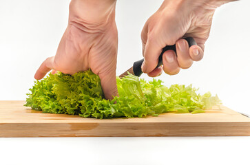 Cutting fresh green salad on a wooden kitchen board. Side view. Female hands with a knife.