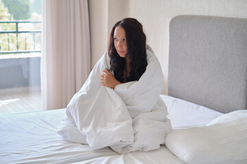 Obraz premium Clasped in a duvet, she contemplates deeply, a natural indoor setting. Reflects the search for comfort in uncertain times, a real moment.