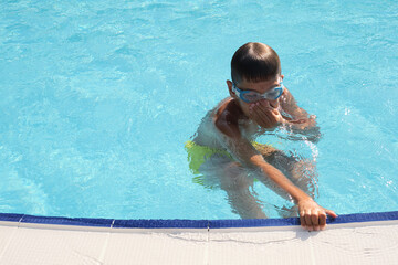 Boy in goggles holds pool edge, water ripples around. Perfect for topics on kids' swimming lessons...