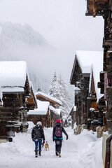 two people walking a dog in a snowy alley in a mountain village