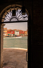 Burano water canal in old town view through old door over colorful mediterranean house neighborhood